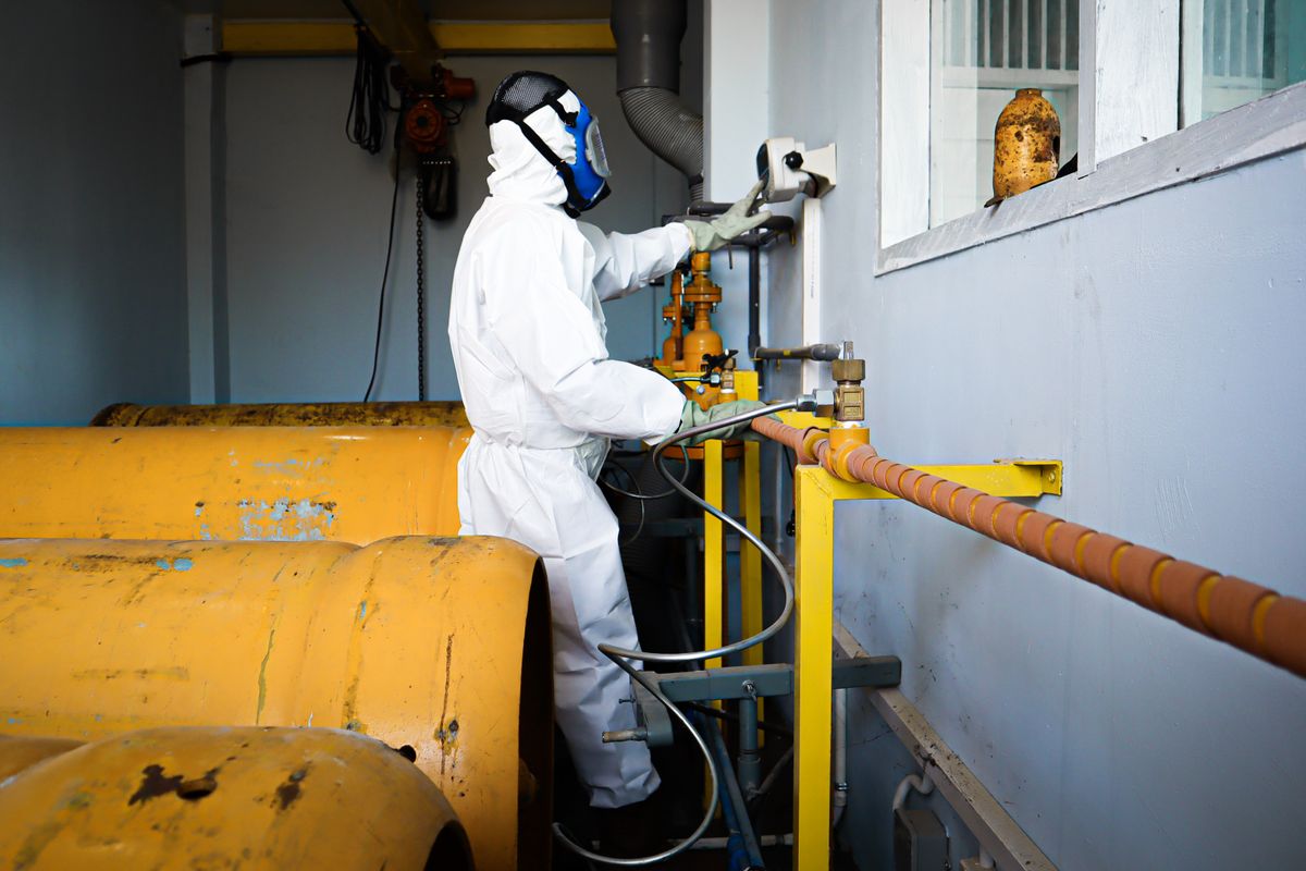 Worker in full protective suit and respirator handling pipes