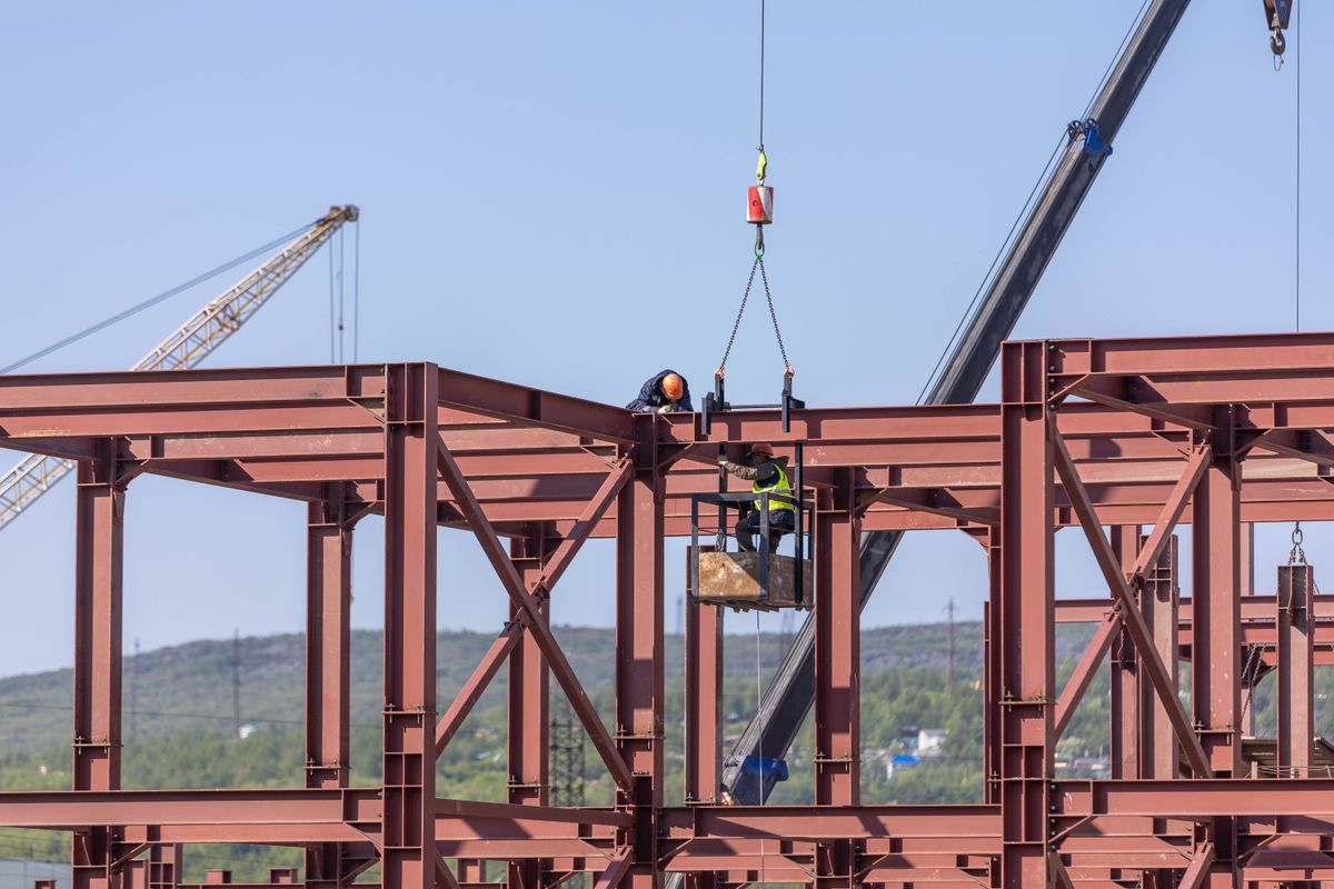 Construction workers assembling a steel frame with cranes