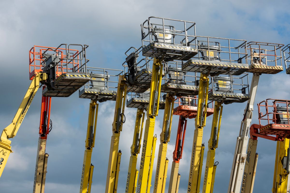 Boom lifts with raised platforms against the sky